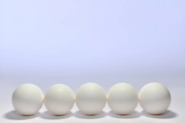 Beş beyaz tavuk yumurtası yan yana dizilmiş. Çerçevenin alt tarafında açık bir zeminde küt yuvarlak bir taban var.. — Stok fotoğraf