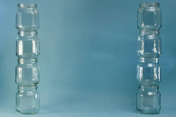 Glass jars are wide lined with two towers vertically against a blue background.