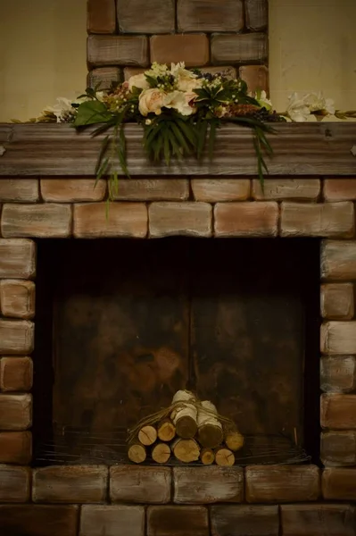Lareira decorativa com troncos de bétula, com um fragmento de chaminé e composição de flores artificiais decoração . — Fotografia de Stock