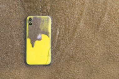 Nah Trang, Vietnam - 12.15.19: Deniz kıyısındaki kumsalda sarı kirli iPhone 11. Tatil gezisi, Apple 'ın yeni cihaz cihazıyla yüzüyor. Su geçirmez cep telefonu. Suya dayanıklı teknoloji testi
