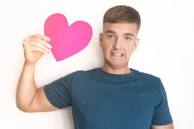 Bekleyen yakışıklı adam, Sevgililer Günü için kalp kartpostalı almış. Beyaz arka planda pembe sevgililer günü tebessümü ile genç, şaşkın, güzel bir adam. Sarışın Avrupalı erkek çocuk