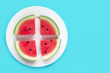 Beyaz yuvarlak tabakta taze olgun kırmızı karpuz dilimleri. Mavi arka planda karpuz kes. Üst manzara, düz yatış. Sağlıklı çiğ vejetaryen yemeği. Boşluğu kopyala, metin için yer aç. Yaz tatili kavramı