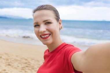 Mutlu, neşeli bir kız, genç bir kadın, selfie çekiyor, fotoğraf çekiyor, cep telefonuyla fotoğraf çekiyor sahilde tatilde, deniz dibinde, gülümsüyor, gülüyor, dışarıda eğleniyor.