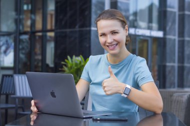 Nah Trang, Vietnam - 02.10.20: Güzel mutlu kadın dışarıda Apple 'ın MacBook dizüstü bilgisayarı üzerinde akıllı Apple Watch ile çalışıyor, iPhone gülümsüyor, başparmağını kaldırıyor, hareket gibi. Bağımsız