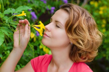 Güzel bir kıza yaklaş, güzel bir kadın kokluyor, kokluyor, aroma soluyor, bahçedeki sarı bahar taze çiçeklerinin tadını çıkarıyor, gözleri kapalı. Çiçekler, çiçekler, doğa, bitki konsepti..