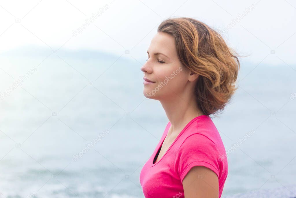 Beautiful girl enjoying walking at good summer sunny weather. Young woman breathing deep, deeply fresh sea air, smiling with eyes closed. Life is good. Relaxed lady dreaming. Calm, meditation concept