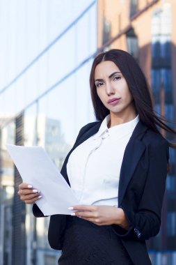 Evraklar, dosyalar, kağıtlar, resmi kıyafetler, takım elbise, beyaz gömlek ve ceket içinde kameraya bakan seksi, ciddi ve seksi bir iş kadınının dikey fotoğrafı. Meşgul genç sekreter kız..