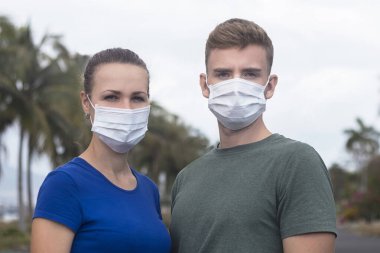 Beautiful serius couple, guy, girl in protective sterile medical mask on face looking at camera outdoors at asian street. Air pollution, virus, new Chinese pandemic coronavirus concept. Man and woman. clipart