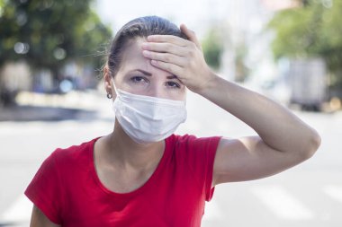 Yorgun bir kız, yüzünde koruyucu steril tıbbi maske takan genç Avrupalı bir kadın. Sıcaklık derecesi var, başını dışarıda tutuyor. Hasta hissediyorum, kötü hissediyorum, acı çekiyorum. Pandemik koronavirüs semptomu