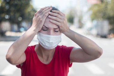 Kızım, yüzünde steril tıbbi maske takan genç Avrupalı bir kadın baş ağrısından muzdarip, elleriyle başını tutuyor. Virüs belirtileri, Çin salgını koronavirüs konsepti. 2019 ncov