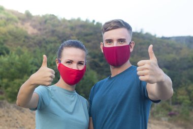 Mutlu mutlu bir çift, erkek, kız, koruyucu maskeli bir adam ve kadın kameranın baş parmağını kaldırıyor, jest gibi. Hava kirliliği, virüs, Çin pandemik koronavirüsü koruma konsepti. 2019-ncov.