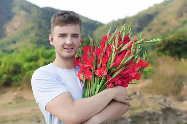 快乐的金发碧眼的欧洲帅哥 年轻浪漫的男人 带着一束美丽的红宝石花 在户外 看着相机 微笑着 花卉概念 — 图库照片