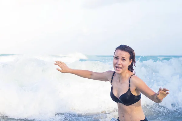 Frightened funny girl flees, runs from a big wave at sea. Danger, dangerous situation while swimming. Scared surprised woman trying to run away from drowning, flood. Summer vacation fun concept.