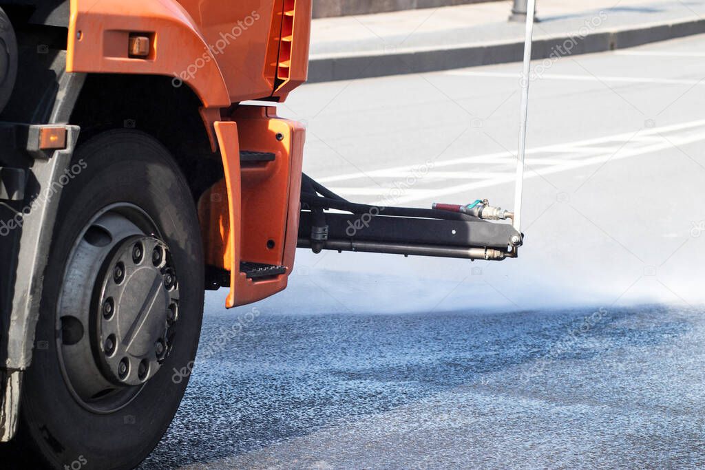 The car washes the streets, asphalt in the city. Road disinfection during coronavirus, covid-19. Street sweeper, watering machine with water.