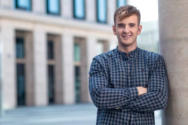Handsome happy cheerful guy, young beautiful European man standing with his hands, arms crossed, looking at camera outdoors, smiling. Copy space, place for text. Positive boy, businessman in a shirt