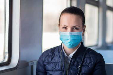 Coronavirus 'a karşı yüzünde tıbbi koruyucu maske takan genç ve ciddi bir kadın. Trende tek başına oturan güzel bir kız, toplu taşıma. Corona virüsü, salgın hastalık, Covid-19, sağlık, seyahat konsepti