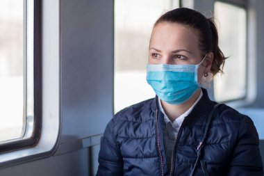 Coronavirus 'a karşı yüzünde tıbbi koruyucu maske takan genç ve ciddi bir kadın. Trende tek başına oturan güzel bir kız, toplu taşıma. Corona virüsü, salgın hastalık, Covid-19, sağlık, seyahat konsepti