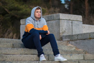 Üzgün üzgün adam, kapüşonlu merdivenlerde oturan, kötü ruh hali yüzünden acı çeken, gelecekteki sorunları düşünen, mesafeye bakan yalnız genç adam. Kırık kalp, başarısızlık konsepti.