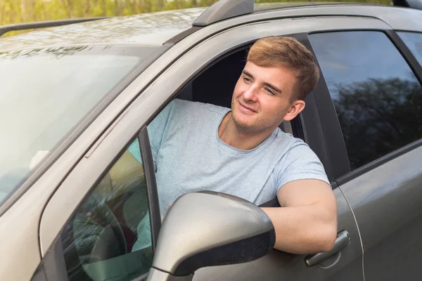 Knappe, vrolijke man, chauffeur, jonge positieve man, rijdend in zijn auto, glimlachend, opvallend uit het raam van de auto. Gelukkige koper van een nieuwe auto die geniet van het rijden. Emotie, geluk, vreugde concept — Stockfoto