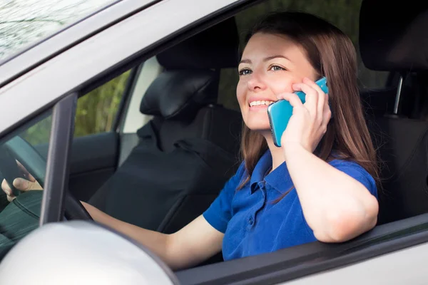 Hermosa chica, mujer joven conduciendo un coche, sonriendo y hablando en su teléfono móvil. El uso de teléfono inteligente durante la conducción de automóviles, al volante. Situación peligrosa, no prestar atención en la carretera — Foto de Stock