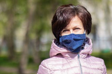 Yüzünde koruyucu maske takmış, orta yaşlı yetişkin bir kadının portresi parkta yürüyen, kameraya bakan bir kadın. Coronavirus, salgın hastalık, virüs Covid-19 konsepti.