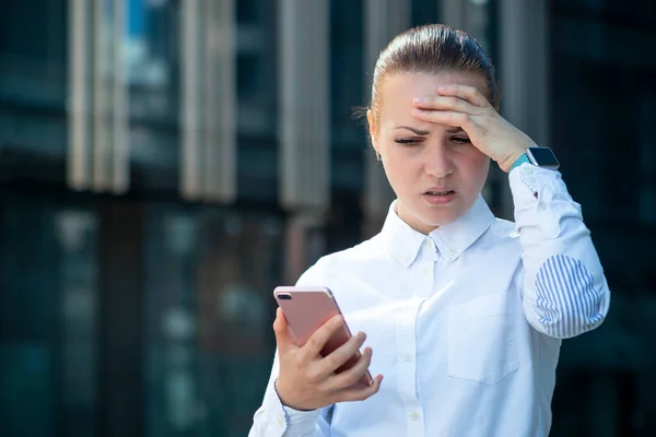Печально расстроенная измученная бизнес-леди, молодая девушка, смотрящая на свой мобильный смартфон, страдающая от плохих негативных новостей, сообщений, держащая голову за руку. Озил, хедлайнер, технологическая концепция — стоковое фото