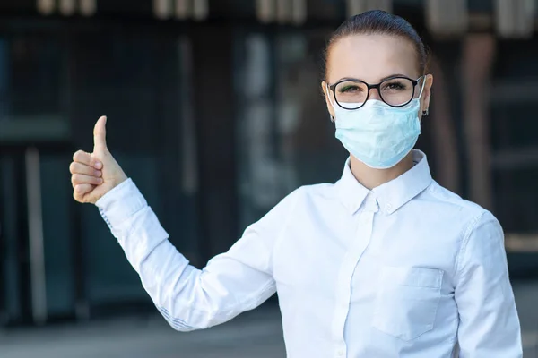 Hermosa mujer de negocios, niña en máscara de protección médica en su cara, en camisa blanca en gafas al aire libre, aparecen pulgar hacia arriba, como gesto. Coronavirus, virus, epidemia, concepto covid-19 — Foto de Stock