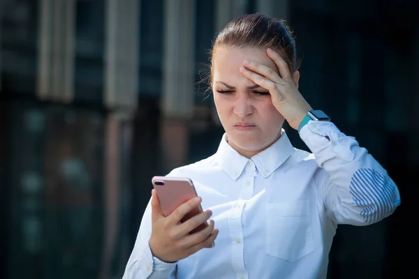 Печально расстроенная измученная бизнес-леди, молодая девушка, смотрящая на свой мобильный смартфон, страдающая от плохих негативных новостей, сообщений, держащая голову за руку. Озил, хедлайнер, технологическая концепция — стоковое фото
