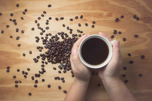 Café preto na mão e grãos de café no fundo textura de madeira . — Fotografia de Stock