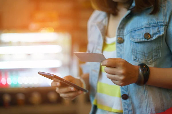 Frau benutzt Smartphone und hält Kreditkarte mit Einkaufszettel in der Hand — Stockfoto