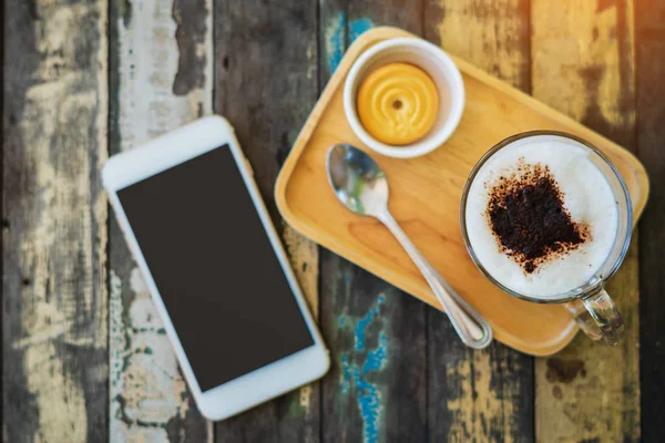 卡布奇诺咖啡与智能手机木材纹理背景。 br — 图库照片