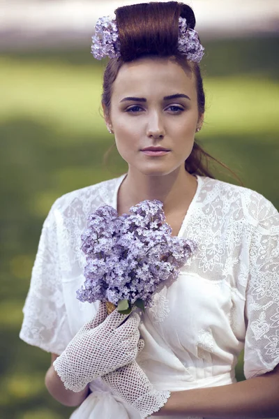 A girl in a white dress with a bouquet of lilac sits on the grass. The bride with a bouquet.