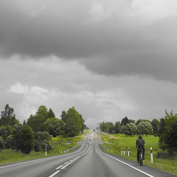 Letonya 'da bir yol resmi. Boş sphalt yolu, kenarlarda bir bisikletçi geziyor.