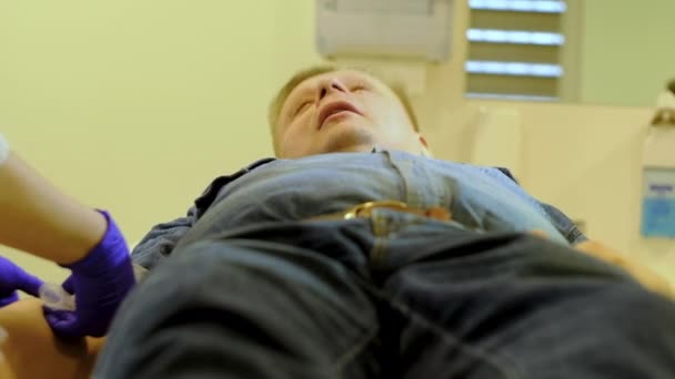 Медсестра дає внутрішньовенну ін'єкцію чоловікові в джинсовому костюмі — стокове відео