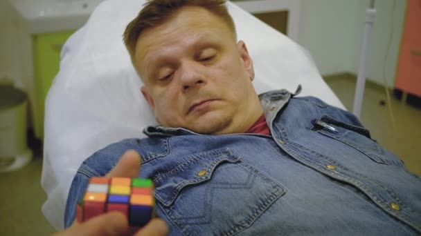 Egy farmer öltönyös férfi hazudik és játszik a Rubik kockában. — Stock videók