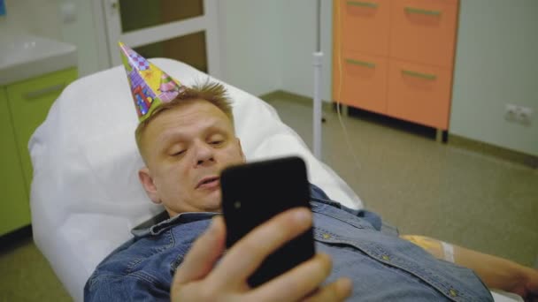En man i jeansdräkt och en festlig mössa tar en selfie på telefonen — Stockvideo