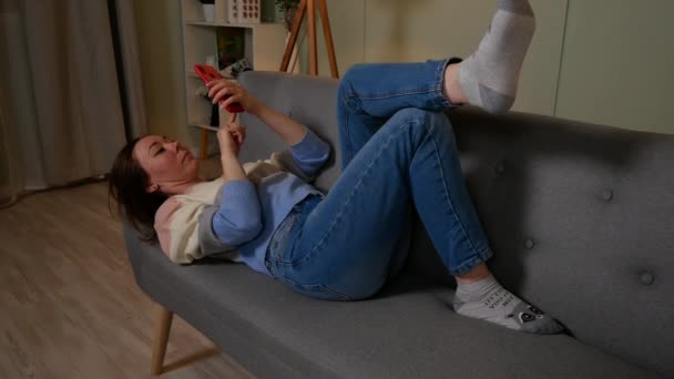 Дівчина лежить на дивані і розмовляє на мобільному телефоні — стокове відео
