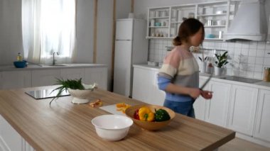 Kız mutfakta dans edip şarkı söylüyor.