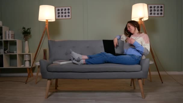 Девушка на диване болтает с помощью ноутбука — стоковое видео