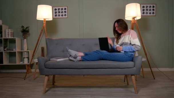 Chica en el sofá llorando, revisando algo en un ordenador portátil — Vídeo de stock