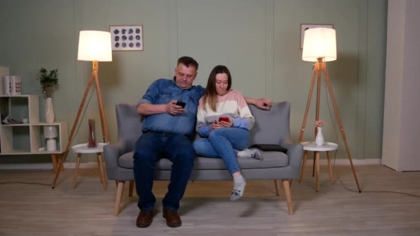 Пара сидит на диване и играет на мобильных телефонах — стоковое видео