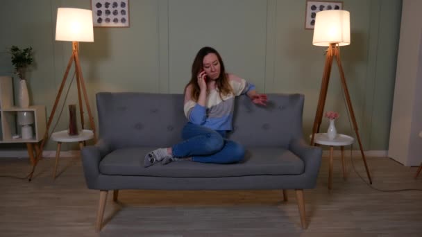 Lány a kanapén a nappaliban beszél mobilon — Stock videók