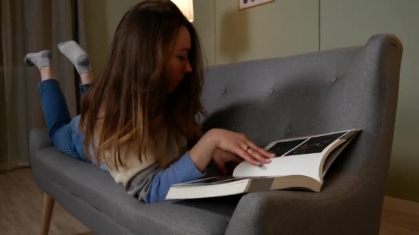Девушка листает журнал и разговаривает по мобильному телефону — стоковое видео