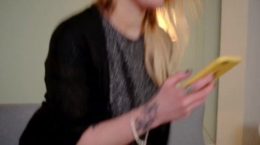 Kanepede oturan kız akıllı telefondan bir şey izliyor.