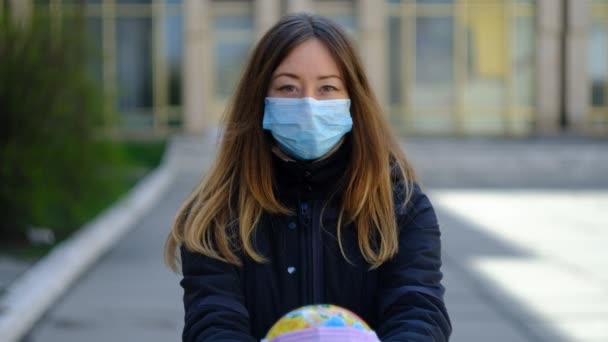 Девушка с длинными волосами в медицинской маске показывает глобус в маске — стоковое видео