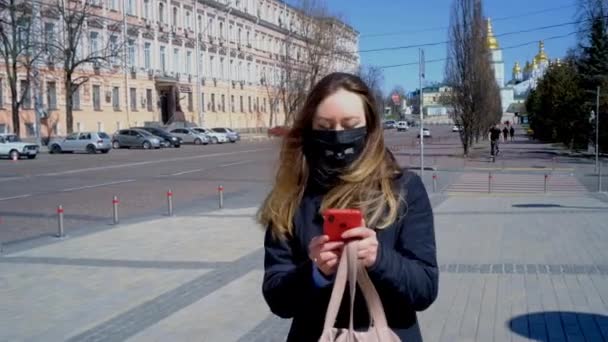 Une fille marche dans la rue avec un masque et répond à un appel téléphonique — Video