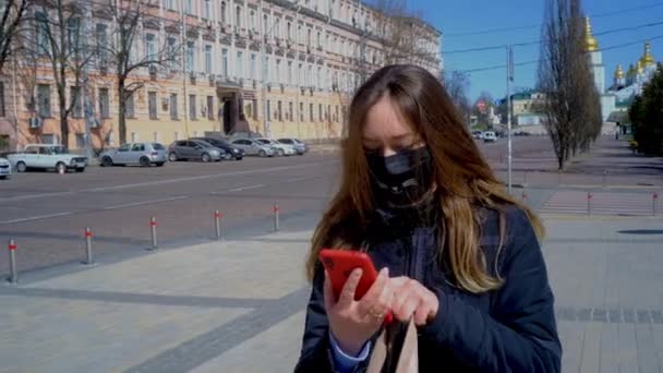 Mujer joven enmascarada camina por la calle y habla en el teléfono inteligente — Vídeo de stock