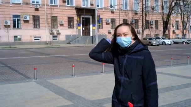 Langhaariges Mädchen in blauer medizinischer Maske läuft über den Platz — Stockvideo