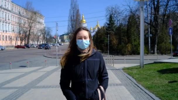 Chica de pelo largo en una máscara médica azul caminando por la plaza — Vídeo de stock