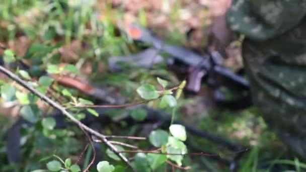 Um homem na floresta com um uniforme militar leva e joga armas Kalashnikov — Vídeo de Stock